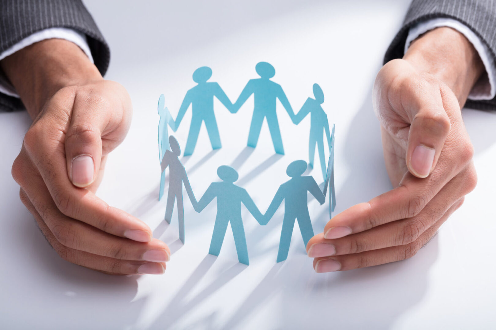 Close-up,Of,A,Businessperson's,Hand,Protecting,Cut-out,Figures,On,Desk Close-up,Of,A,Businessperson's,Hand,Protecting,Cut-out,Figures,On,Desk
